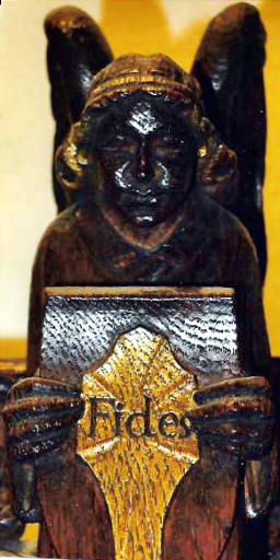 Angel holding a wooden shield on which are engraved the shield of faith with the word Fides in the centre