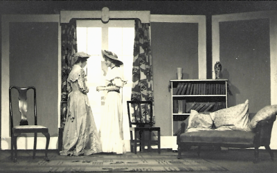 Two female actors addressing each other in a large reception room