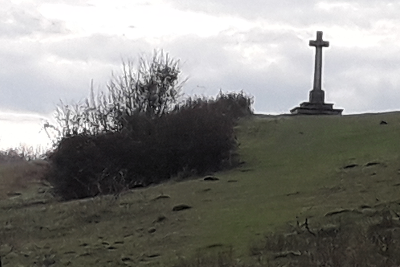 View up a hillside with gorse buch on left and memorial to right on top of hill