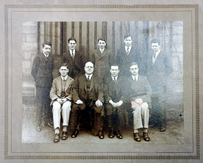 Formal photograph five boys standing behind four people seated
