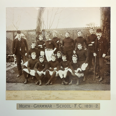 Formal photograph showing six boys standing in front of four in a middle row with five seated cross-legged in front and two masters, one on either side