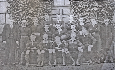 Formal photograph showing seven players standing in front of three players who are in turn in front of four seated players with Sergeant Dillon on the left and Mr W.B. Crump on the right of the back row