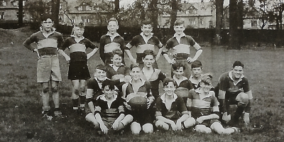 Informal photograph showing five boys standing behind two rows of six and four boys seated on the grass