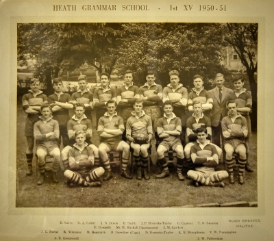 Formal photograph showing eighteen players of the 1950/51 Rugby Team in three rows, nine standing with Mr Birchall between the two at the right hand end of the row, seven seated and two seated crosslegged at the front