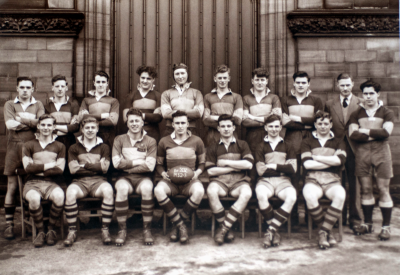 Formal photograph showing sixteen players of the 1952/53 Rugby Team in two rows of seven seated and eight standing with Mr Burchall to the right of the back row and one other player standing to the right of the seated row