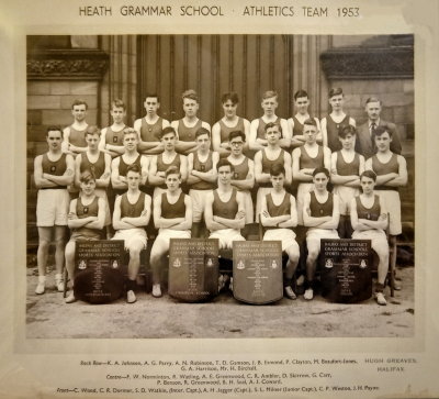 Formal photograph showing three rows of athletes, two rows standing with Mr Birchall to the right of the back row and one row seated with four trophies in front of them
