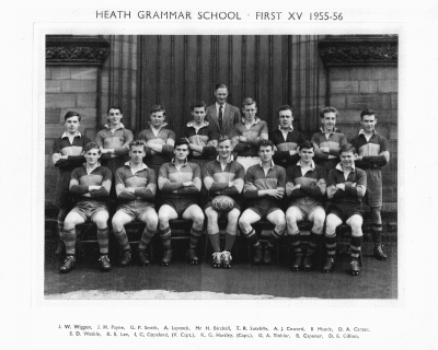 Formal photograph showing fifteen players of the 1955-6 First XV in two rows of seven seated and eight standing with Mr H. Birchall behind the back row