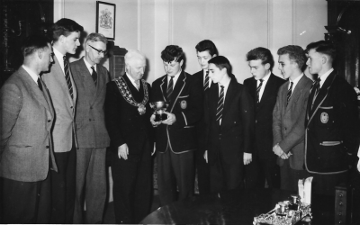 Semi-circle of staff and players with G.P. Smith showing the trophy to the Mayor